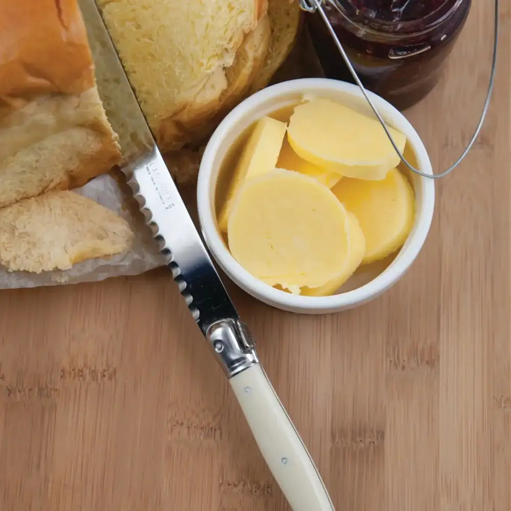 Butter knife with slices of butter on a wooden cutting board next to bread and jam.