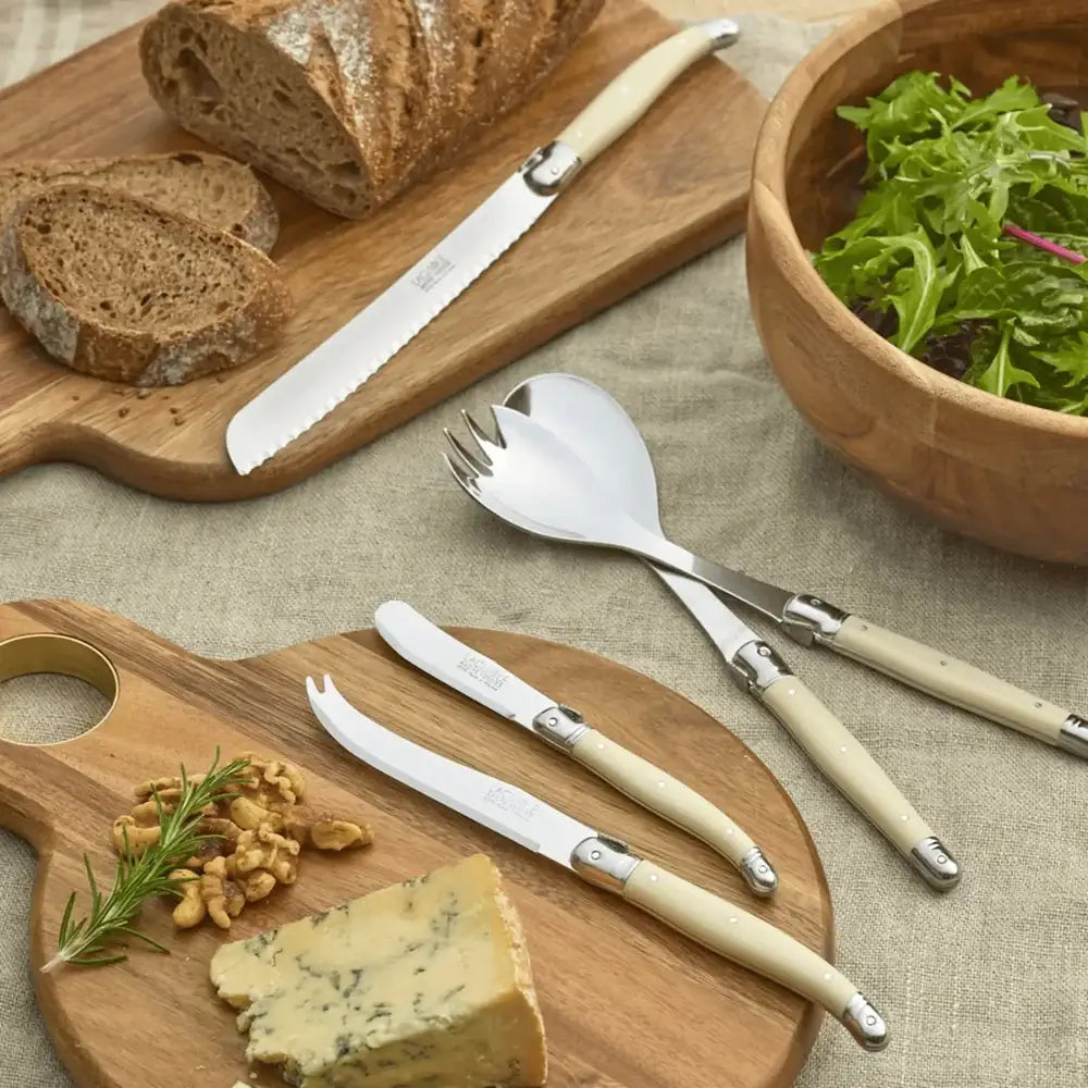 Wooden cutting board with bread, cheese, and a bowl of salad, accompanied by silver and cream-colored cutlery.