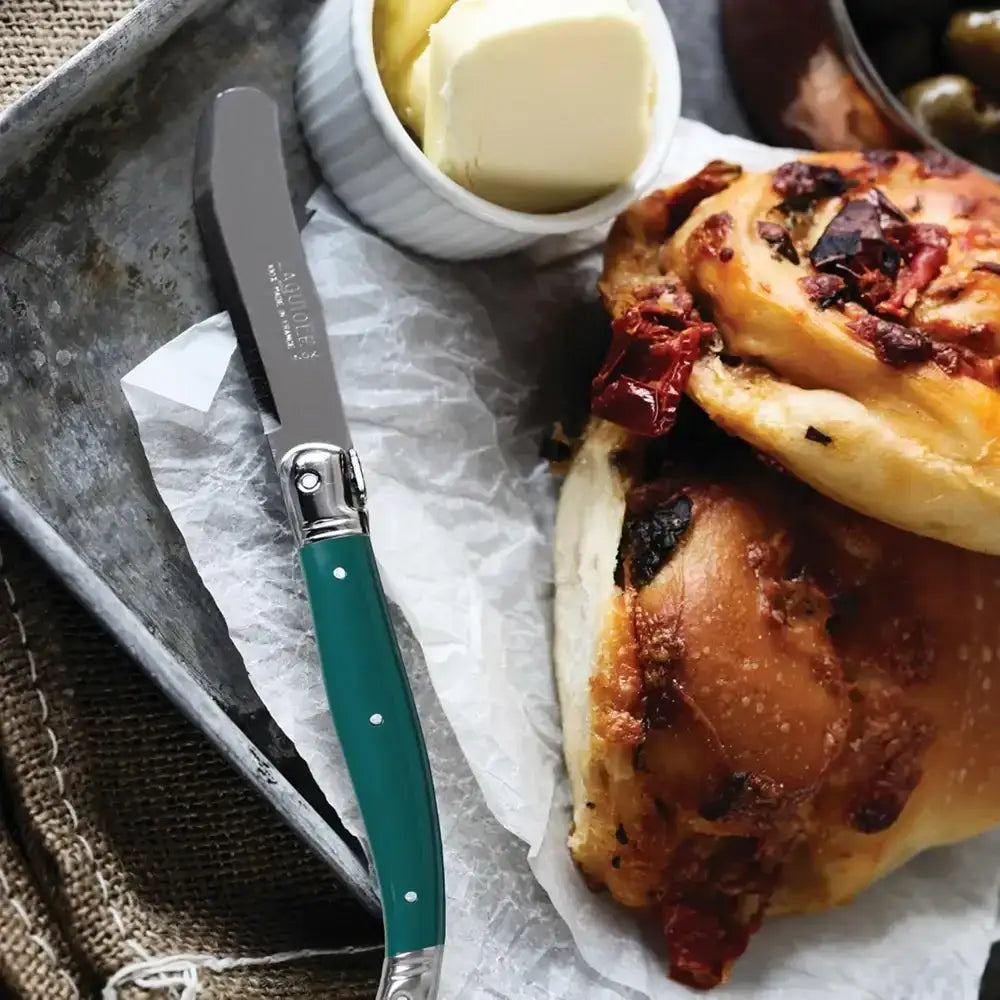 Baked dish with a spreadable topping, knife, and butter on a rustic surface