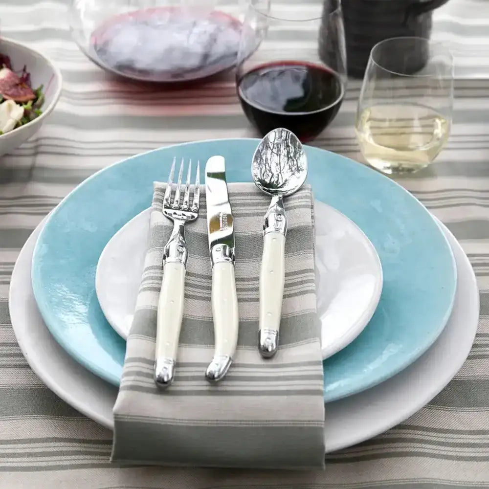 Dining table setting with blue plates, silverware, and a striped cloth.