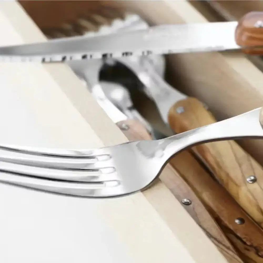 Close-up of a set of silver cutlery with wooden handles on a white surface.