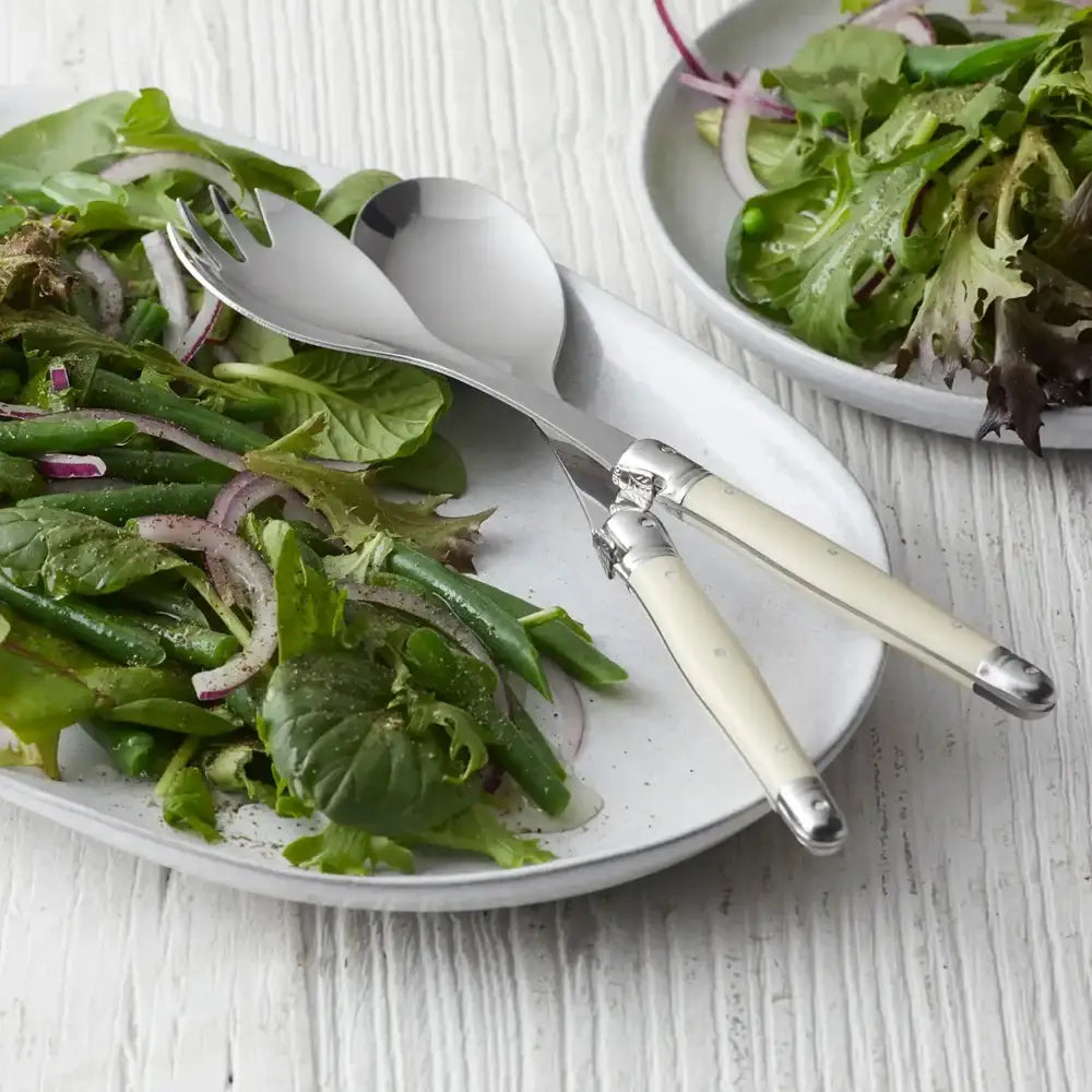 Salad tongs on a plate of green salad with onions on a wooden surface