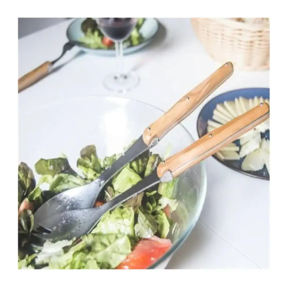 Wooden-handled salad servers in a bowl of salad on a dining table.