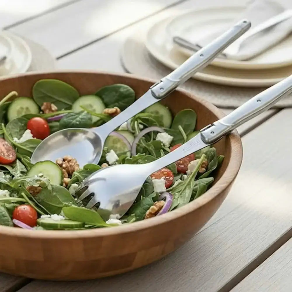 Wooden bowl of salad with silver utensils on a wooden table