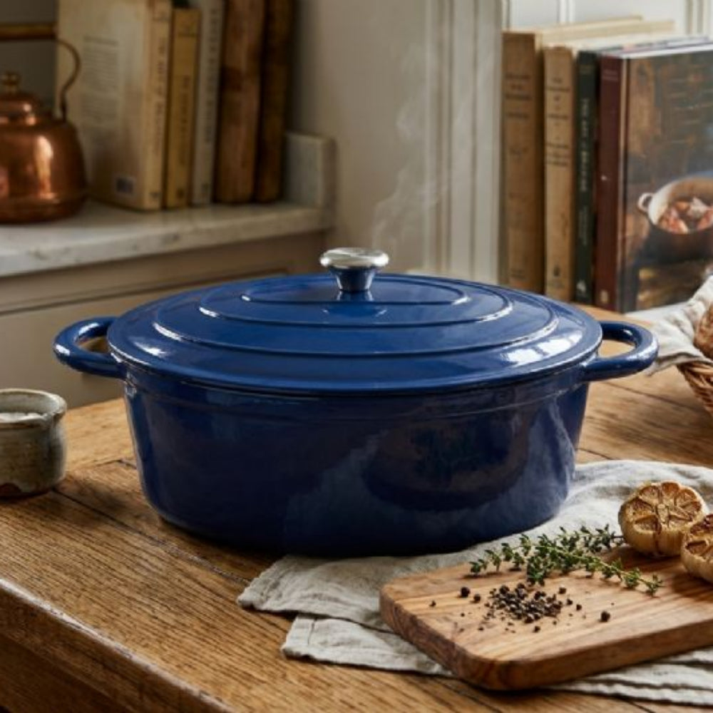 Blue enameled cast iron casserole pot on a wooden kitchen counter with bread and herbs.
