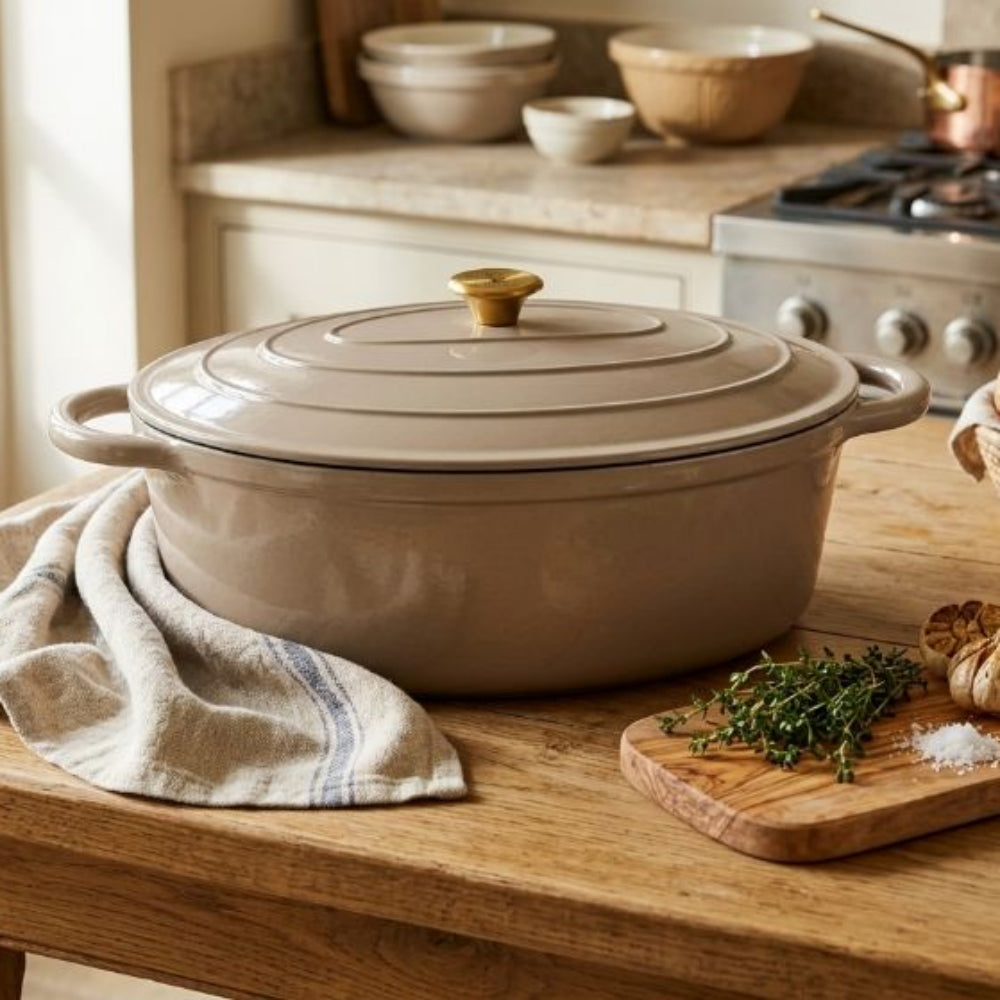 Beige casserole dish on a wooden kitchen counter with bread and herbs.