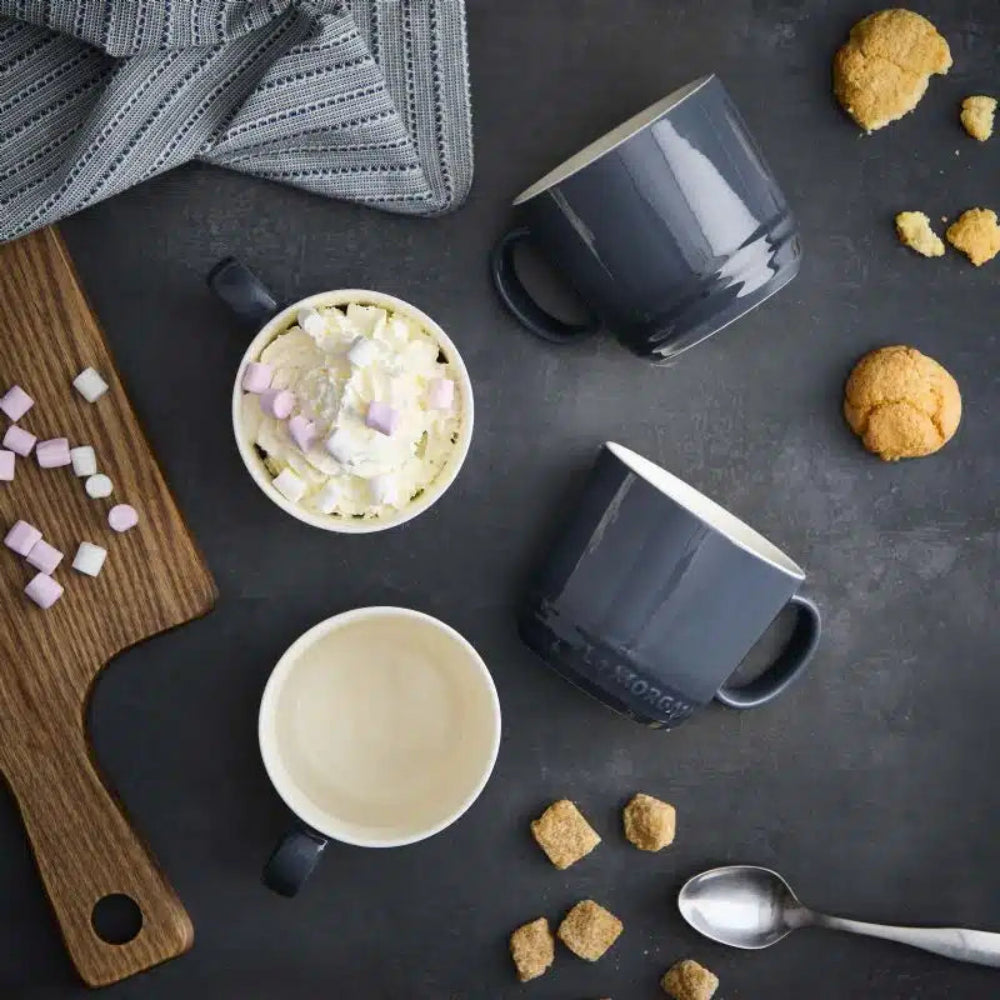 Mugs with hot chocolate, marshmallows, and cookies on a dark surface