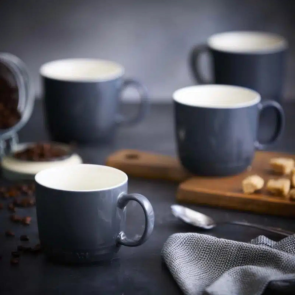 Black mugs on a dark surface with coffee beans and sugar cubes.