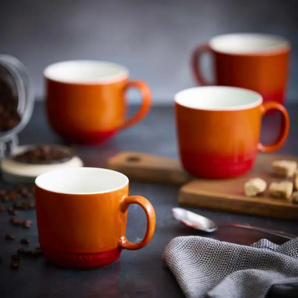 Set of orange mugs on a dark surface with coffee beans and a spoon.