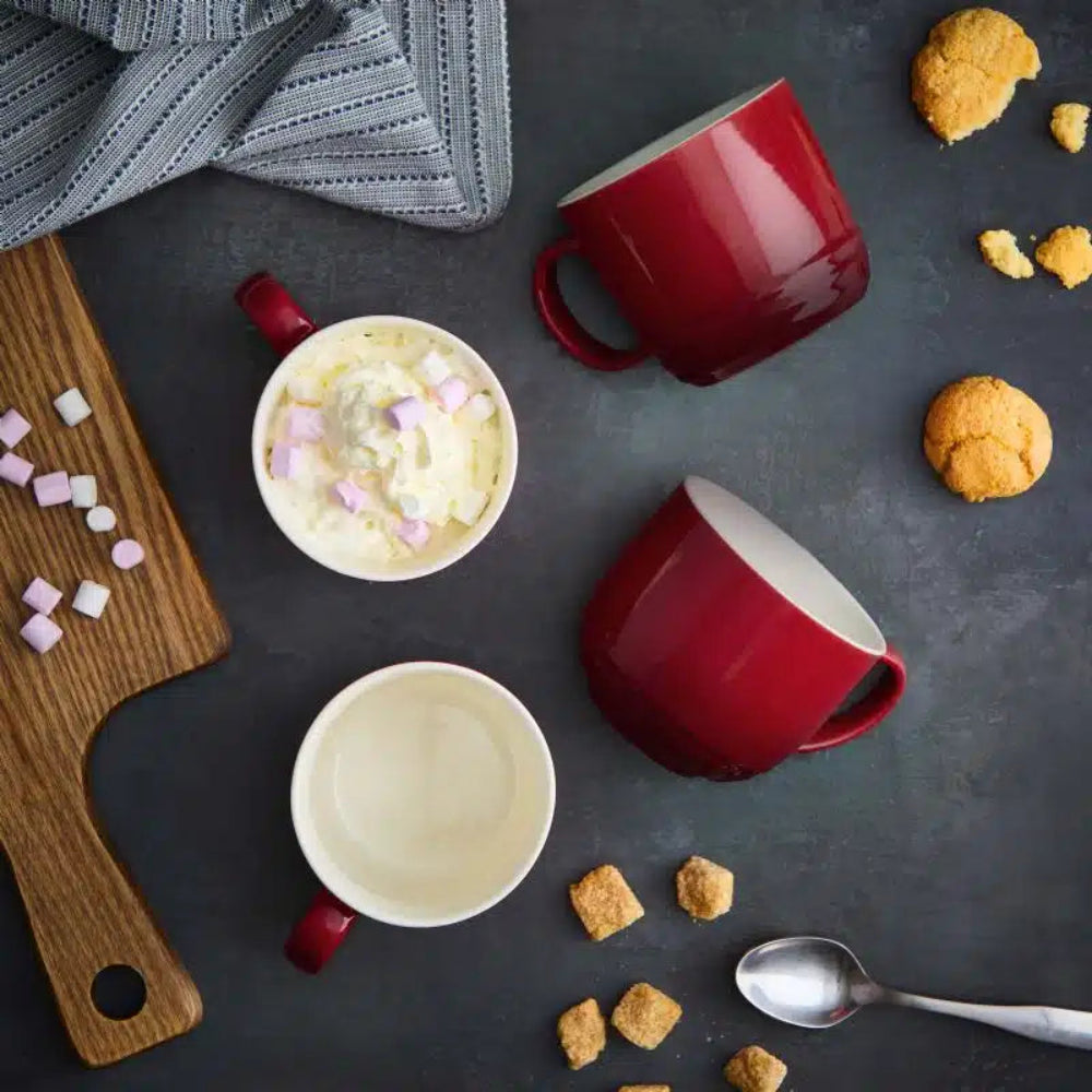 Red and white mugs with hot chocolate and cookies on a dark surface