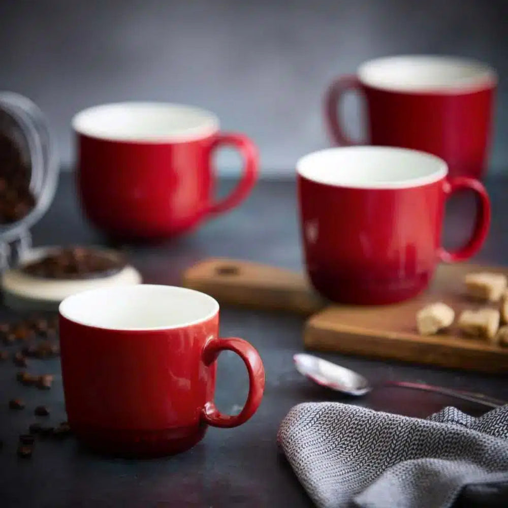 Red mugs on a dark surface with coffee beans and a spoon.