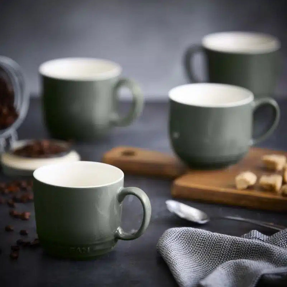 Set of green mugs on a dark surface with coffee beans and sugar cubes.