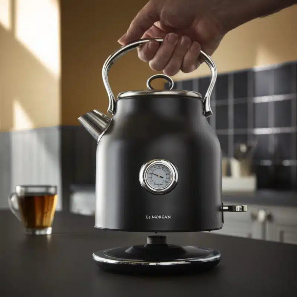 Black electric kettle with a hand holding the handle, placed on a kitchen counter.