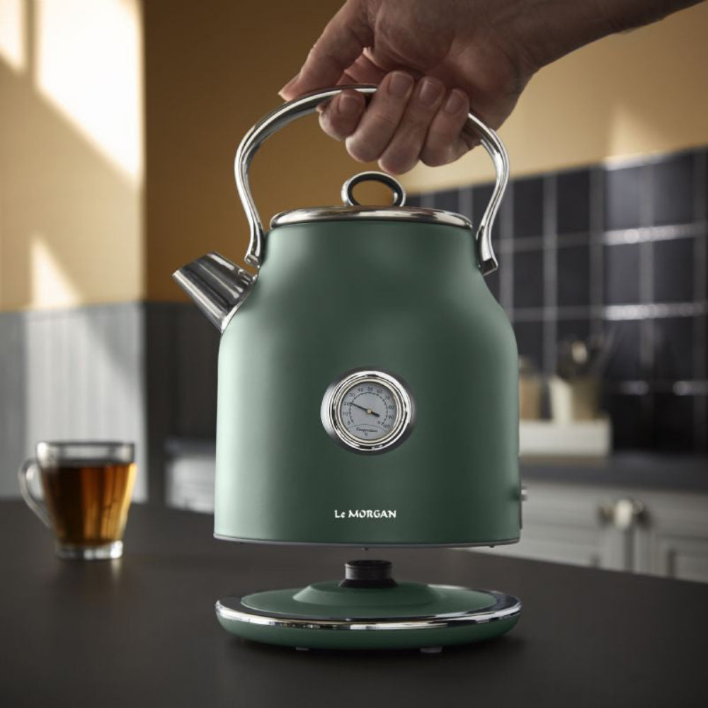 Green electric kettle with a hand holding its handle, set against a kitchen background.