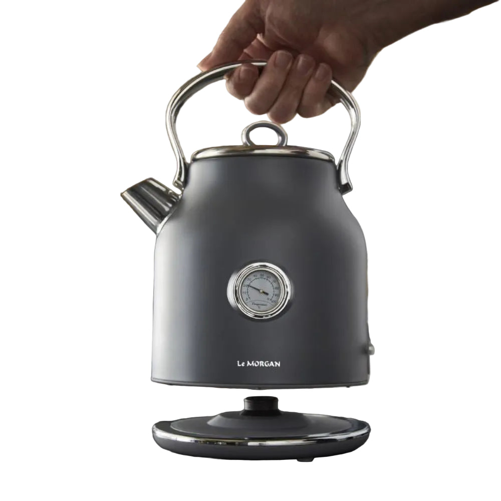 Grey electric kettle with a hand holding its handle, set against a kitchen background.