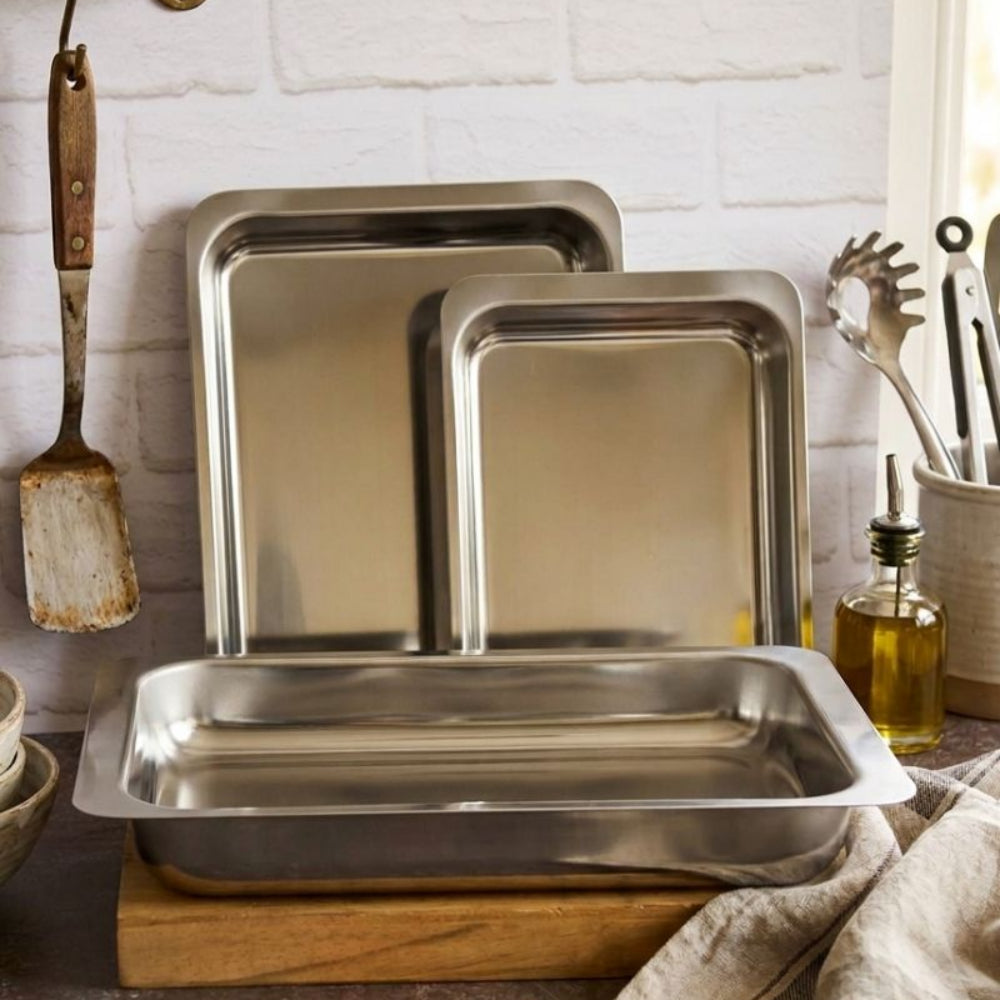 Set of stainless steel baking trays on a kitchen counter with utensils in the background.