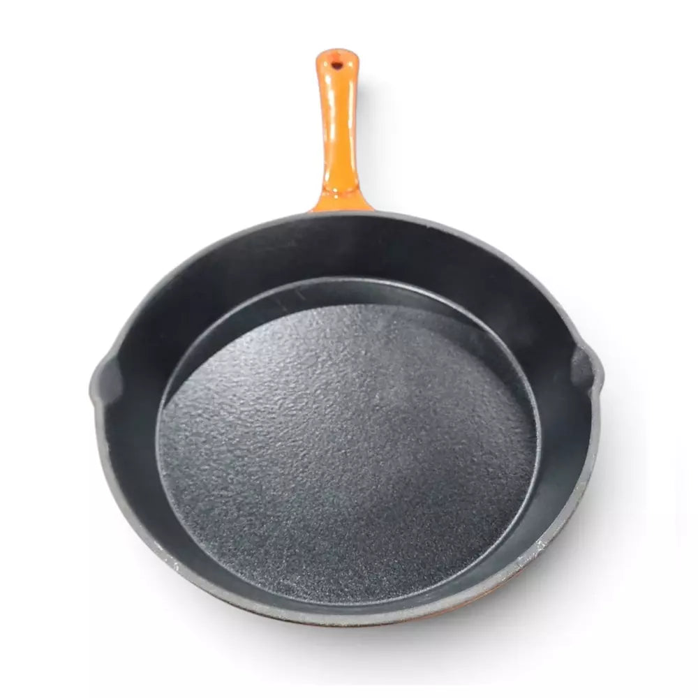 A cast iron skillet with a dark textured interior and exterior, featuring a bright orange enamel handle on a clean white background.