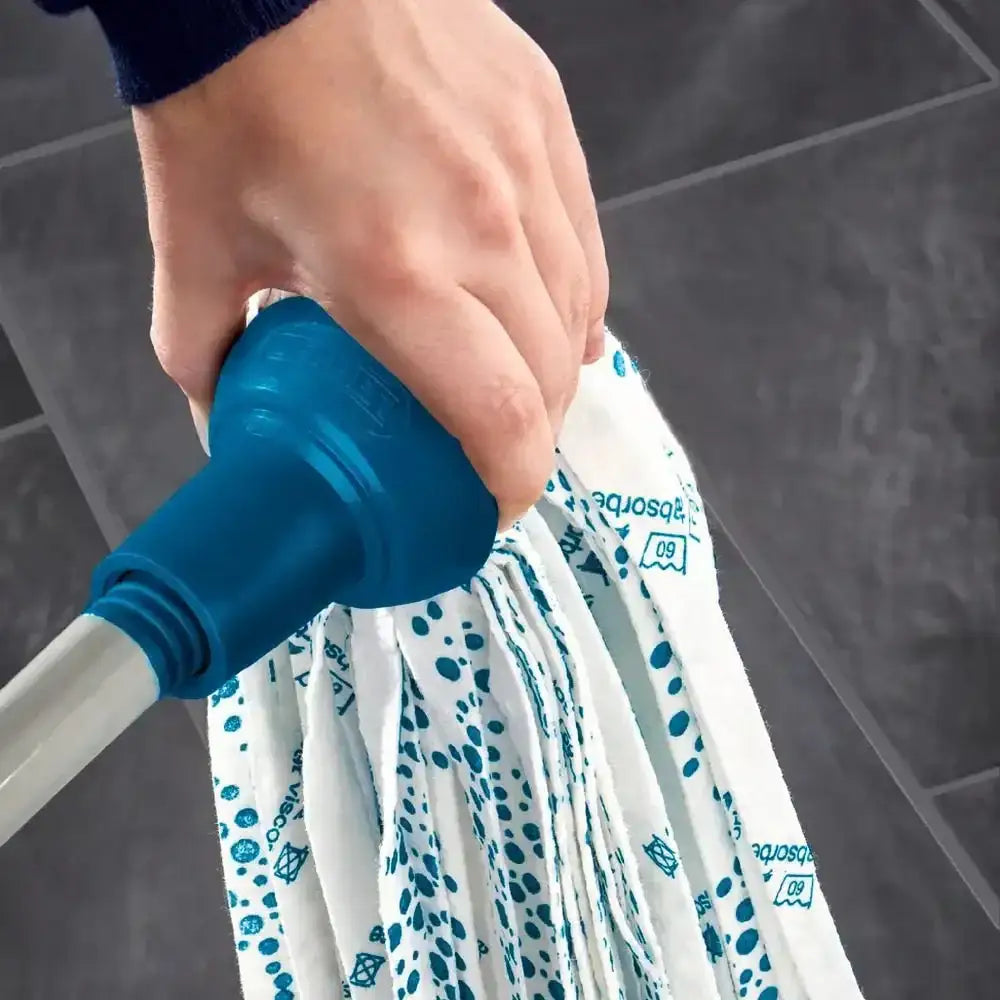 Hand holding a blue and white mop with a patterned head on a tiled floor.