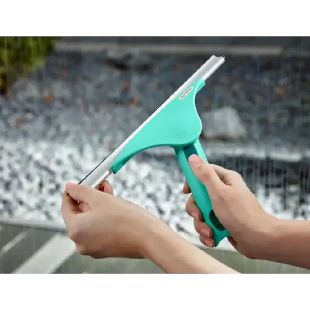 Teal window cleaning tool held by hands with a blurred outdoor background