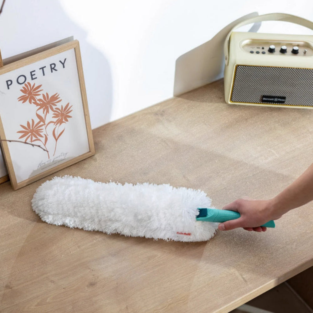 Person using a duster on a wooden surface with a picture frame and radio in the background