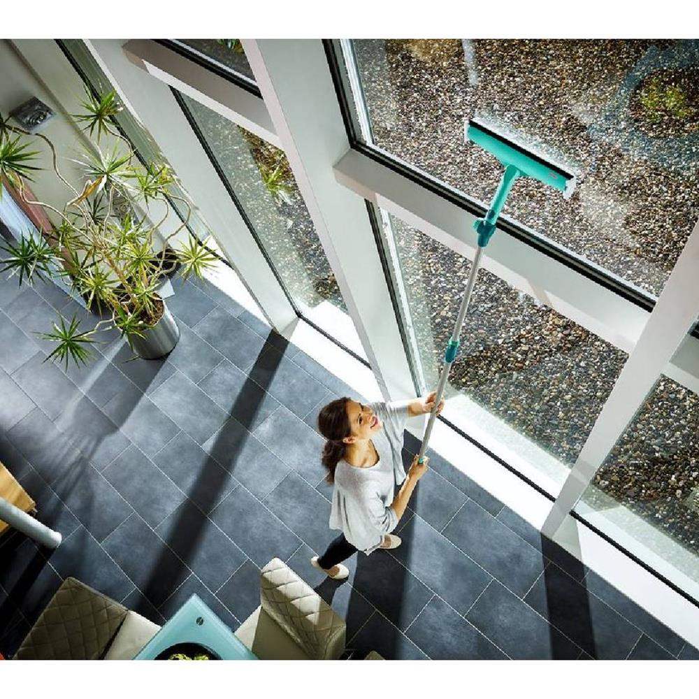 Person cleaning a large window with a squeegee in a modern indoor setting.