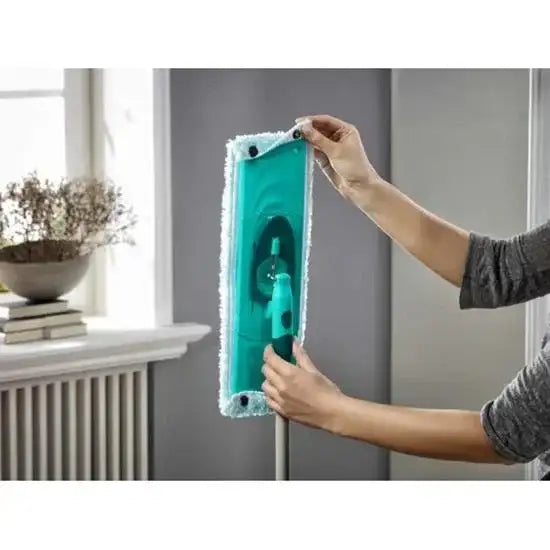 Person holding a green cleaning tool with a textured pad in a room setting.