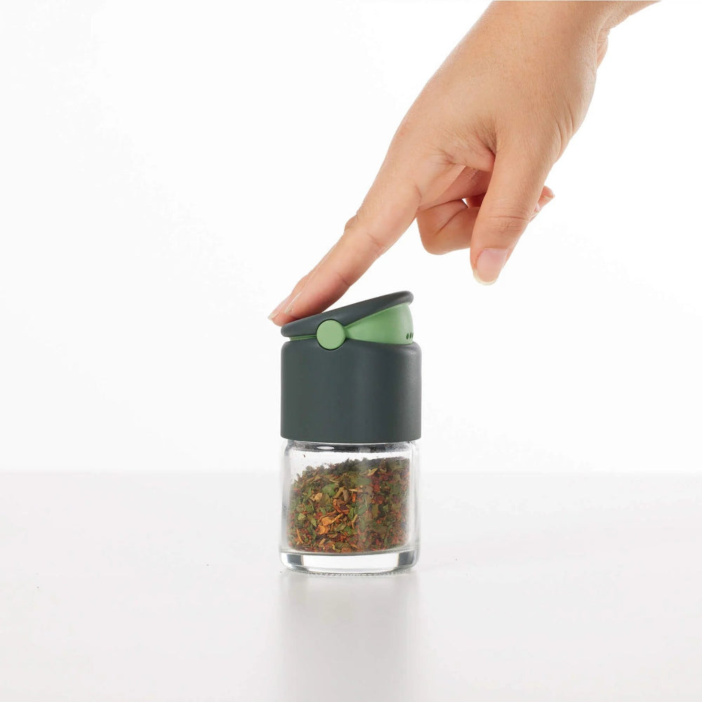 Hand opening a small spice grinder filled with spices on a white background