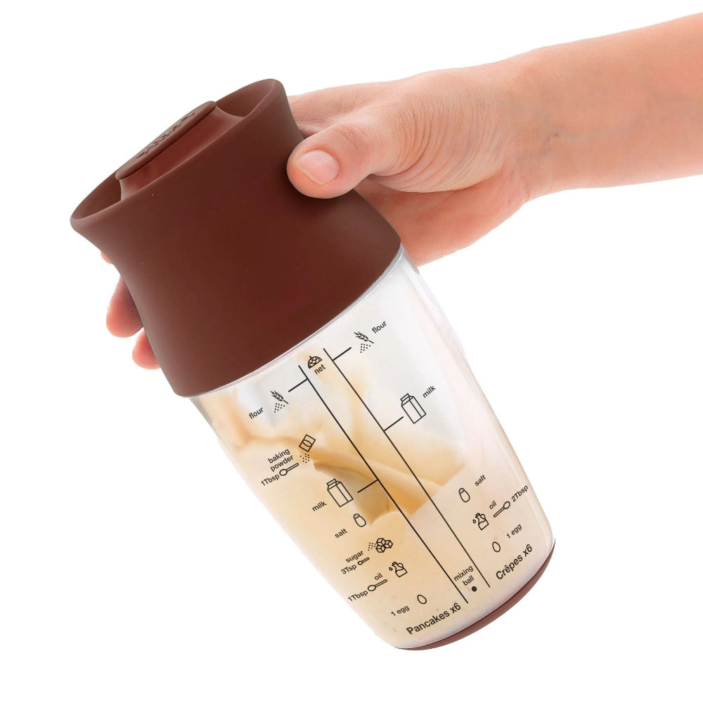Person shaking a pancake batter mixer with a white background 