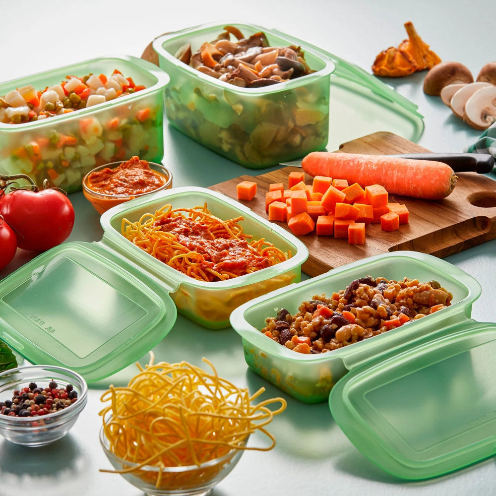 Assortment of food with green containers and a cutting board on a white surface 