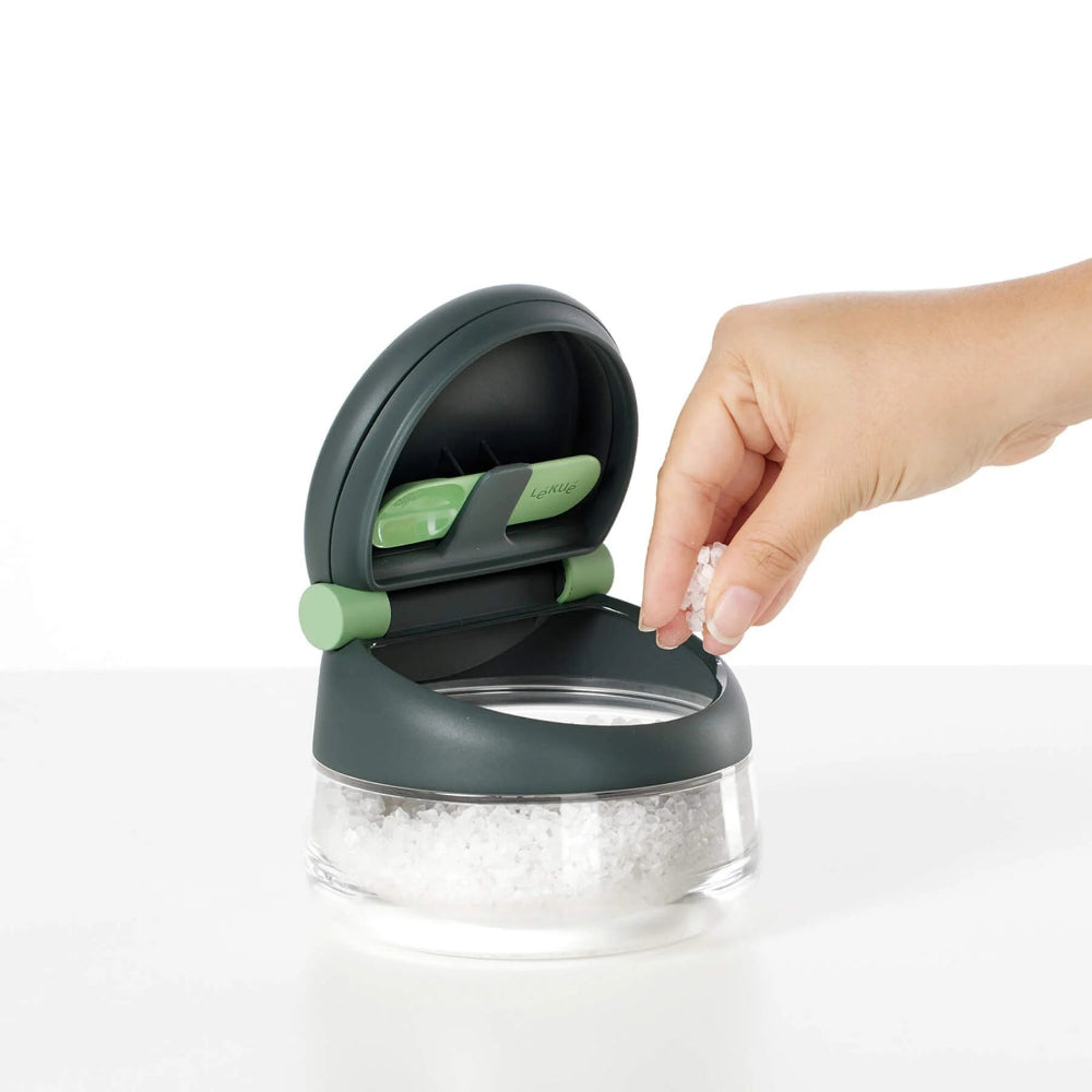 Person grabbing a pinch of salt from a clear container 
