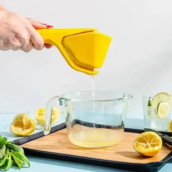 Hand squeezing lemon with yellow juicer into glass measuring cup on kitchen countertop