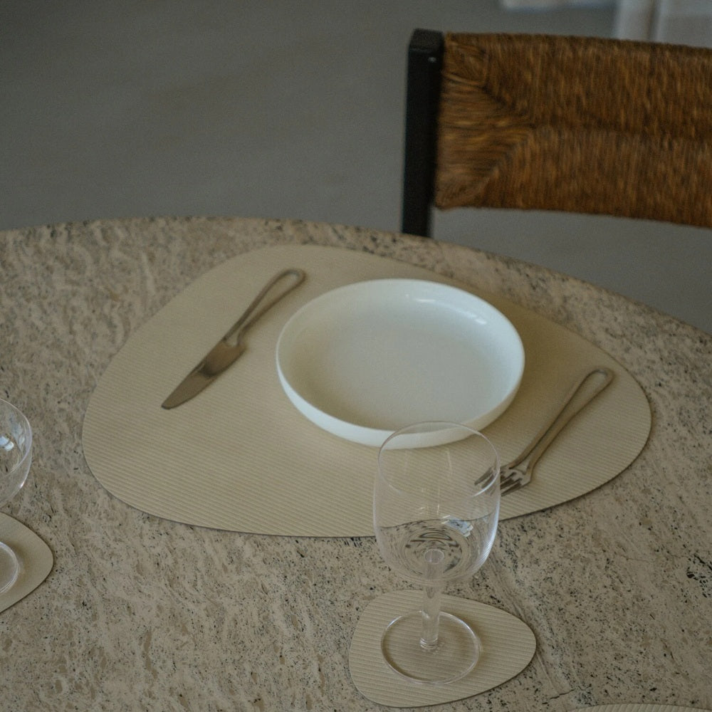 Dining table setting with a white plate, glass, and cutlery on a textured surface.