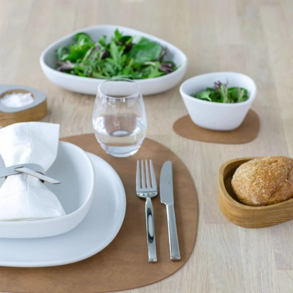 Dining table setting with plates, cutlery, and a bowl of salad on a wooden surface.