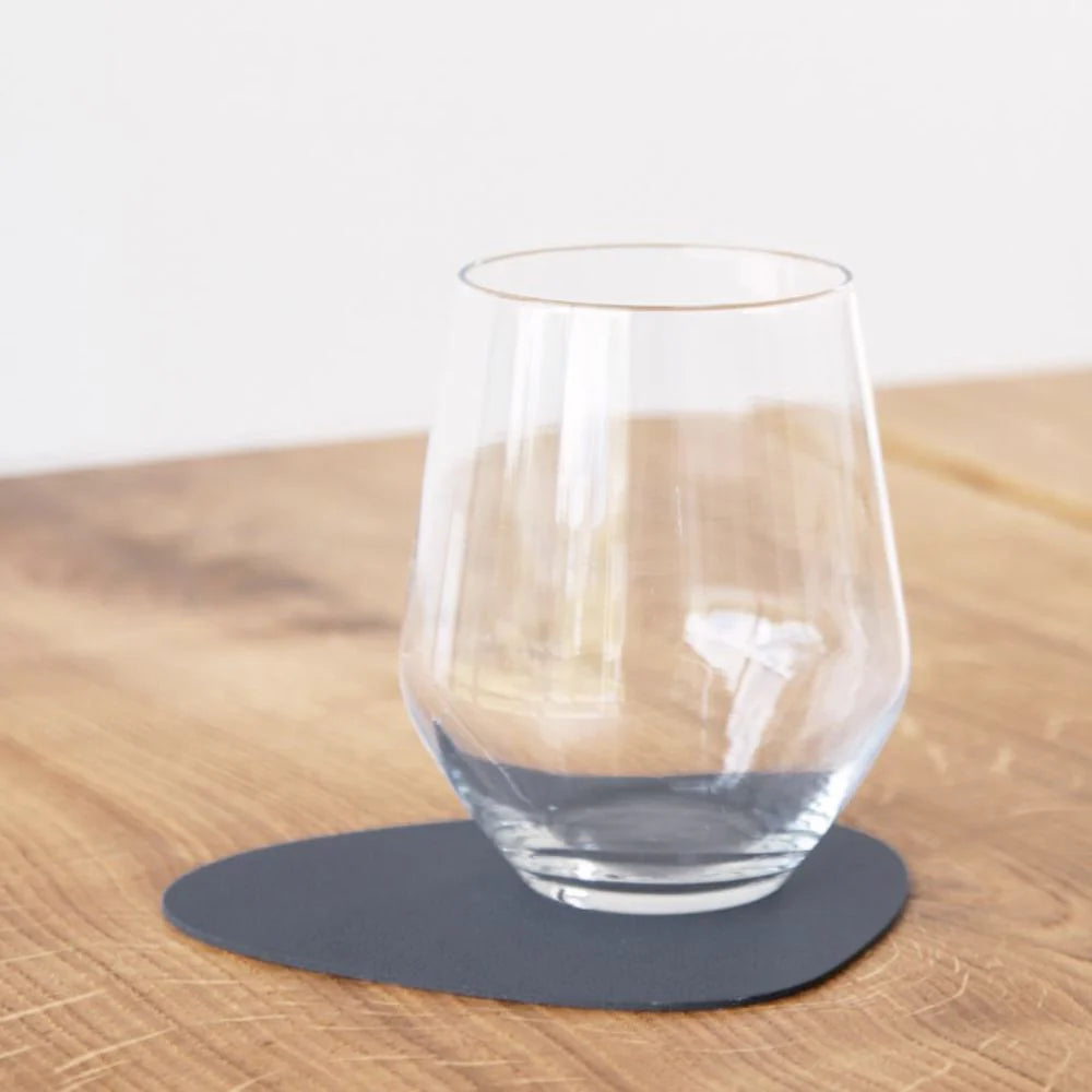 Clear glass on a dark gray coaster on a wooden surface