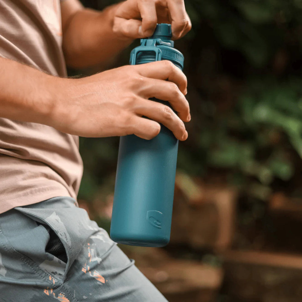 Person holding a blue water bottle outdoors with a natural background