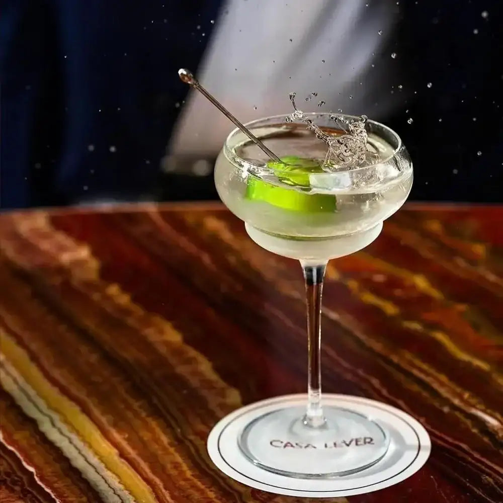 Cocktail in a glass with a lime wedge on a wooden coaster, featuring the Casa Lover brand.