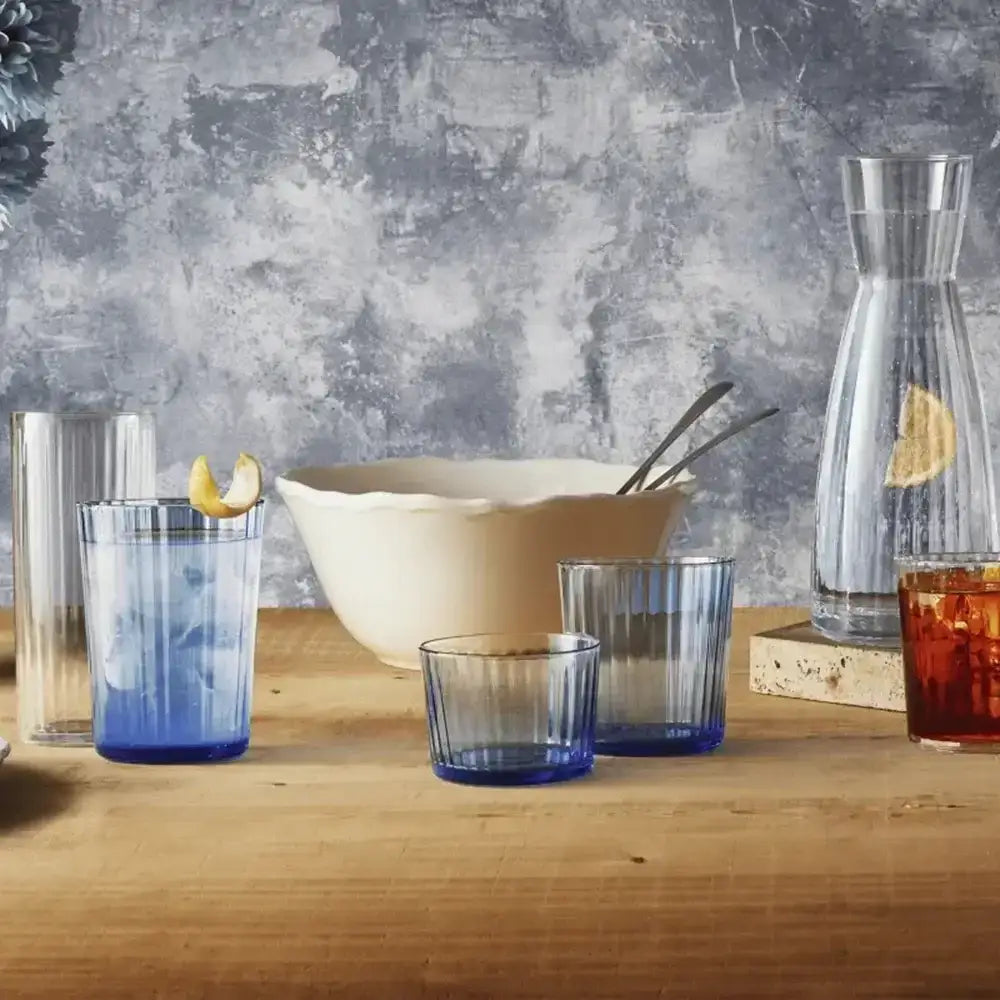 Set of blue glass tumblers on a wooden surface with a textured gray wall background.