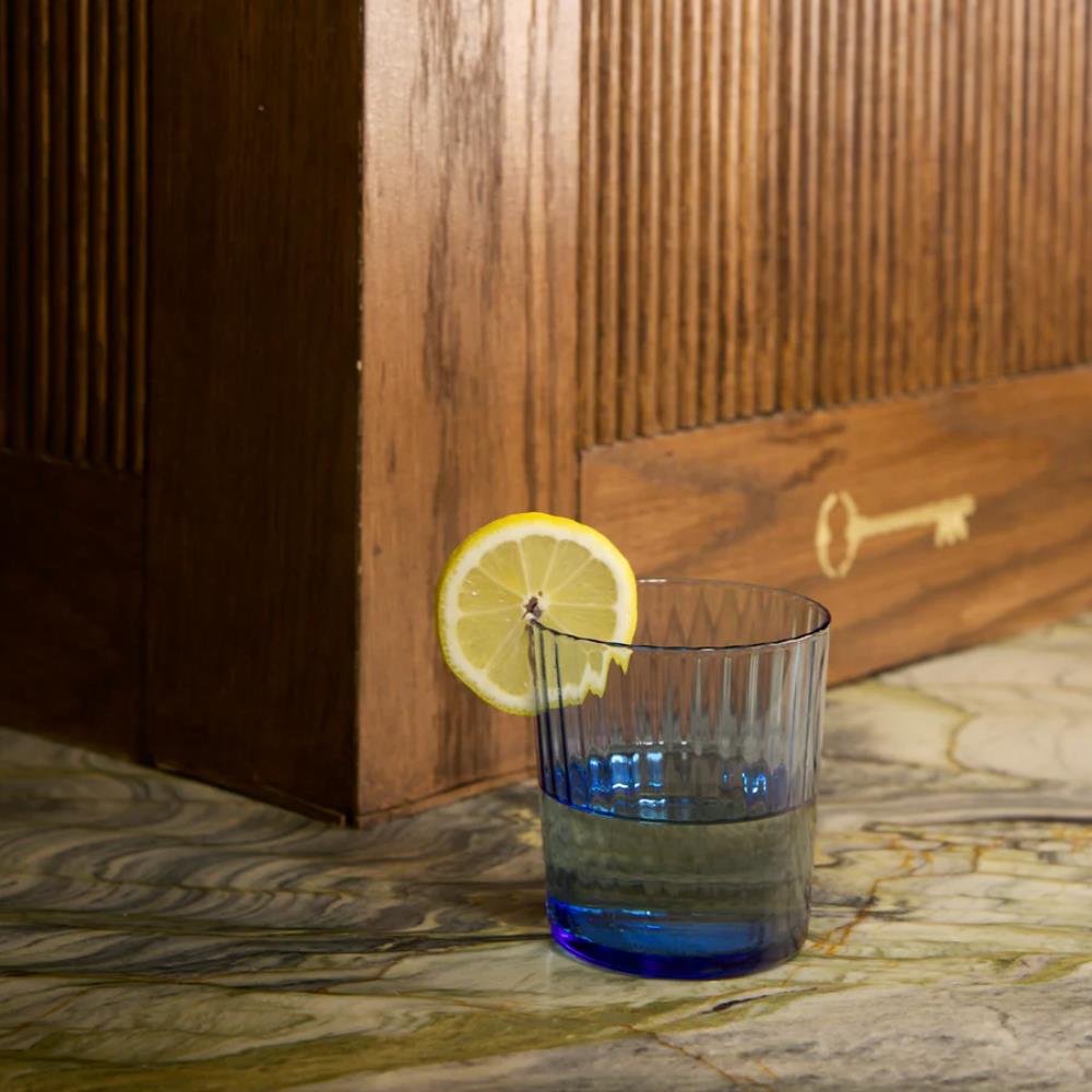Blue glass with a lemon slice on a marble surface with wooden paneling in the background