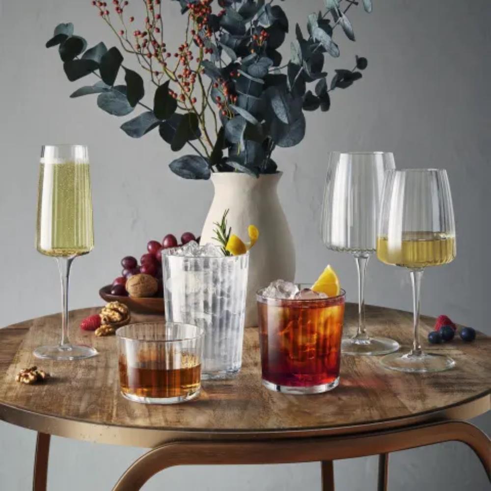 Table with various glasses of drinks and a vase with greenery on a gray background