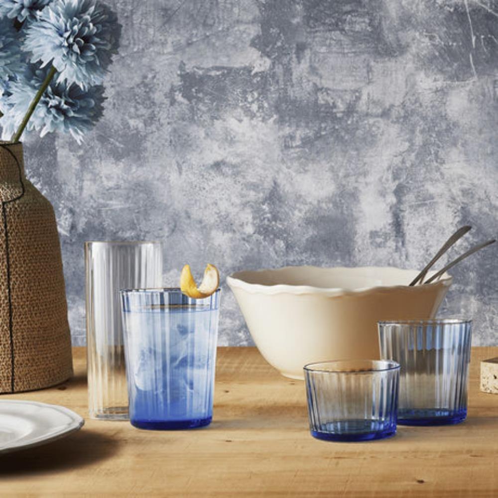 Blue glass tumblers on a wooden table with a textured gray wall in the background
