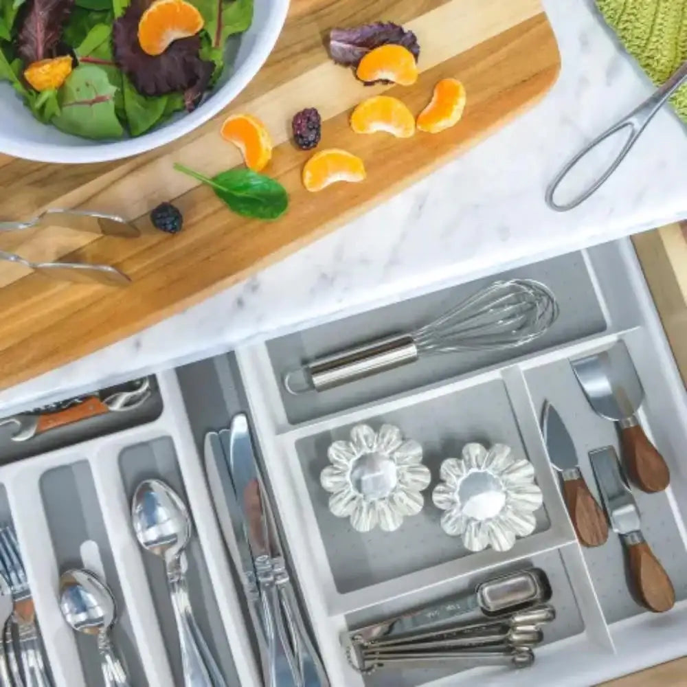 Open drawer with silverware organizer, cutting board with salad and oranges, and a plate of salad on a marble surface.