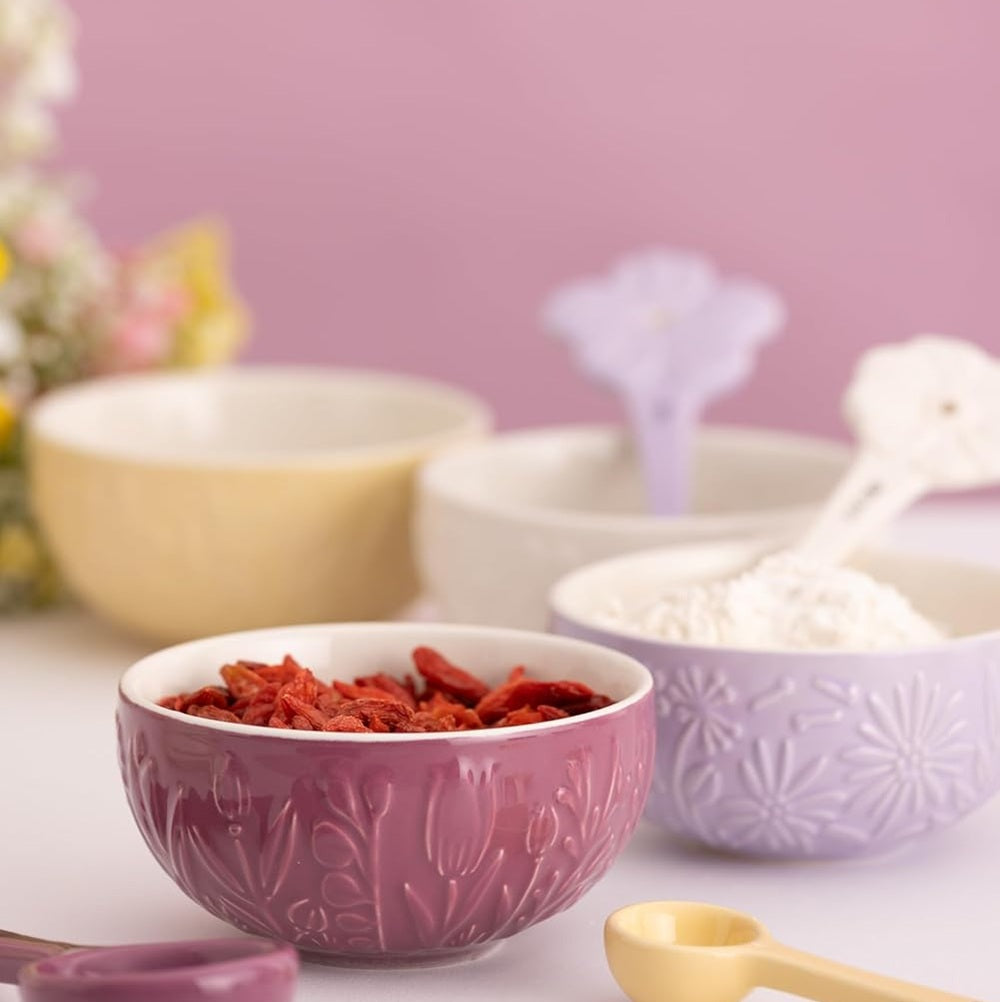 Purple bowl with red dried herbs on a table with other bowls and a pink background