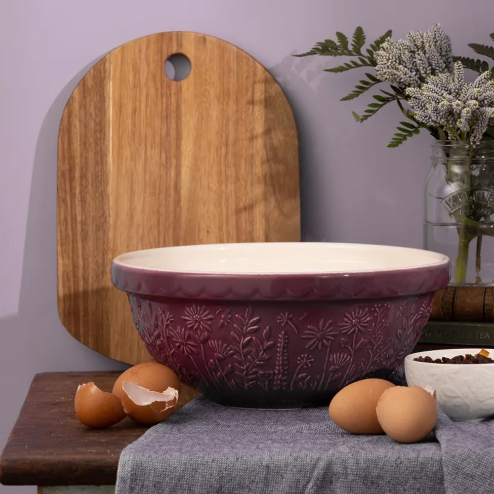 Purple mixing bowl on a kitchen counter with a cutting board and eggs