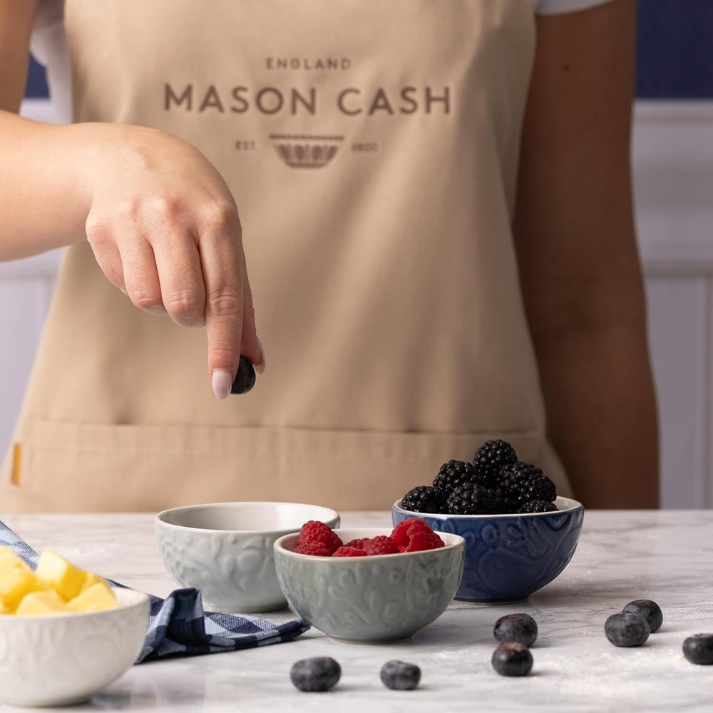 Person wearing a Mason Cash apron with bowls of fruit on a table