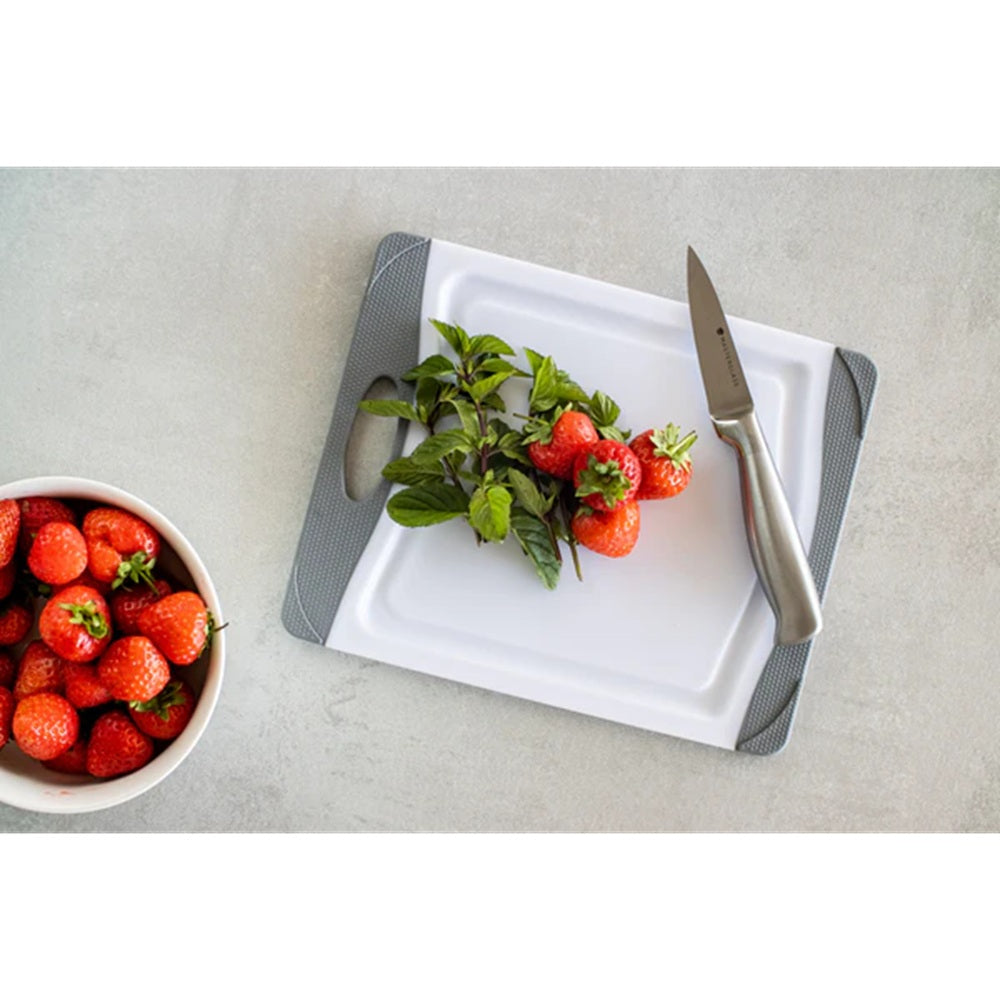 Strawberries on a cutting board with a knife and a bowl of strawberries on a light gray surface