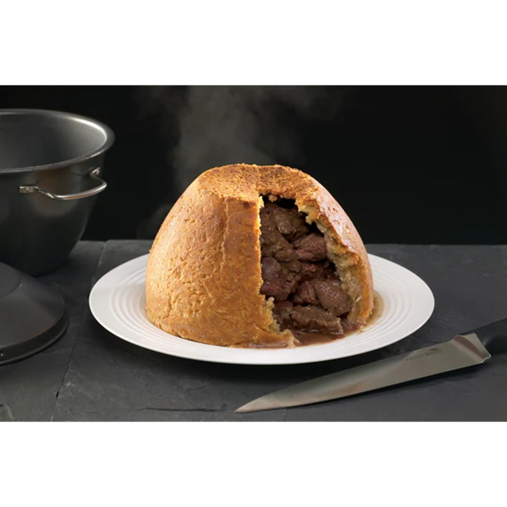 Steamed pudding with meat filling on a white plate, knife nearby