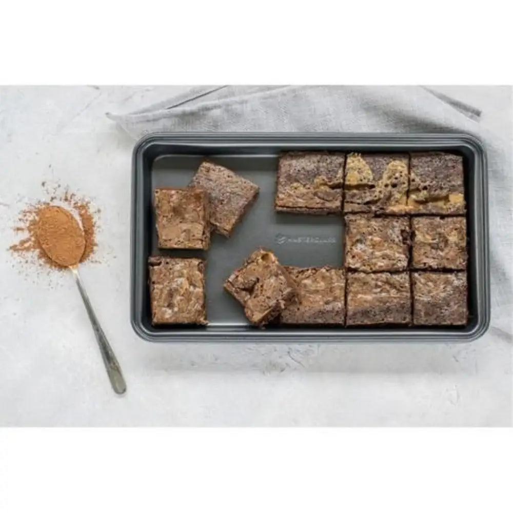 Brownies on a baking tray with a spoonful of cinnamon next to it on a light gray surface.