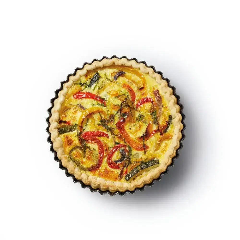 Vegetable tart with red peppers and green herbs on a white background