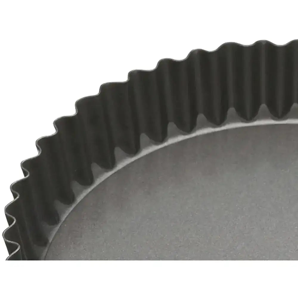 Close-up of a black quiche dish with a ribbed edge on a white background