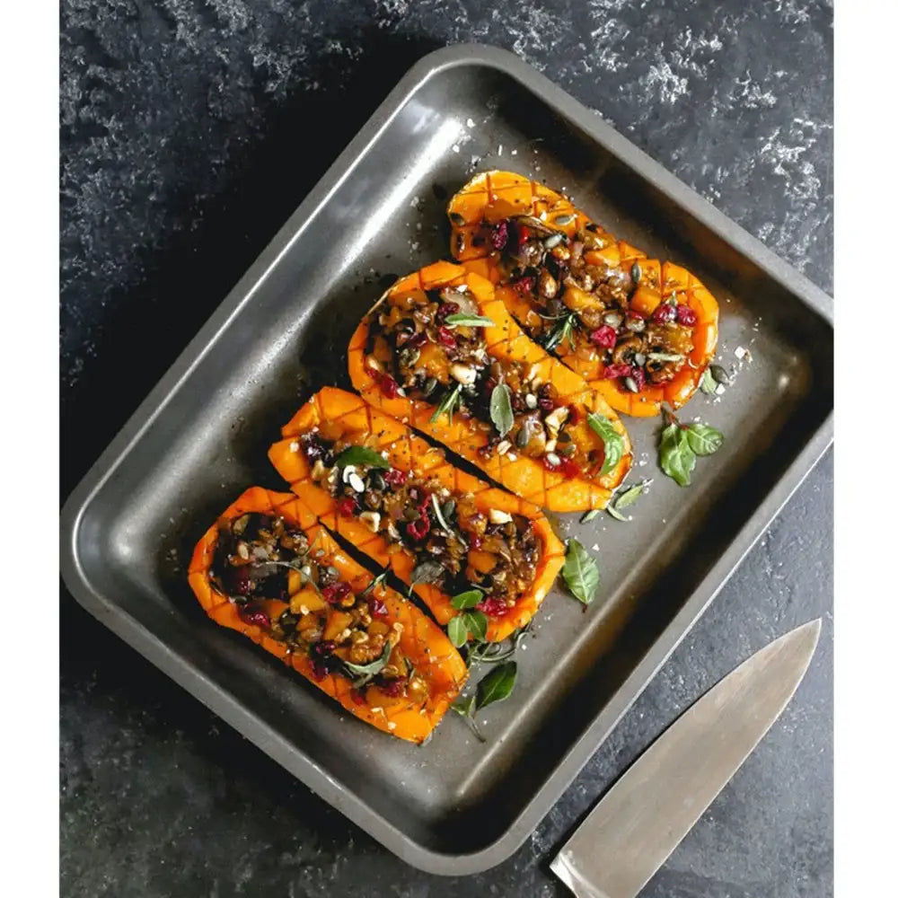 Roasted butternut squash planks with toppings on a baking tray with a knife beside it.
